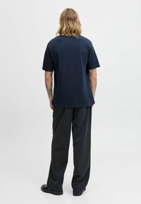 Jūrinės medvilnės T-shirt su trumpomis rankovėmis, apvaliu kaklu ir laisvu siluetu, derinama su tamsiai pilkais plačiais kelnais ir juodais batais.