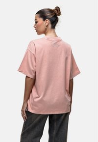 Różowa, oversize'owa koszulka wykonana z bawełny, z krótkimi rękawami, okrągłym dekoltem oraz małym wytłoczonym logo na plecach.
