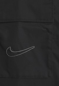 Black fabric with a stitched white Nike swoosh logo on a pocket with visible seam lines.