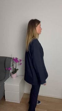Blazer de riscas azul-marinho com um corte descontraído, combinado com calças de riscas a condizer. Tecido suave e hardware mínimo. Ambiente interior com uma planta.