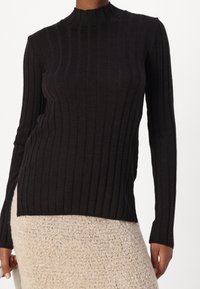 Maglione nero a coste con collo alto e maniche lunghe, dotato di spacchi laterali allungati e una silhouette aderente.