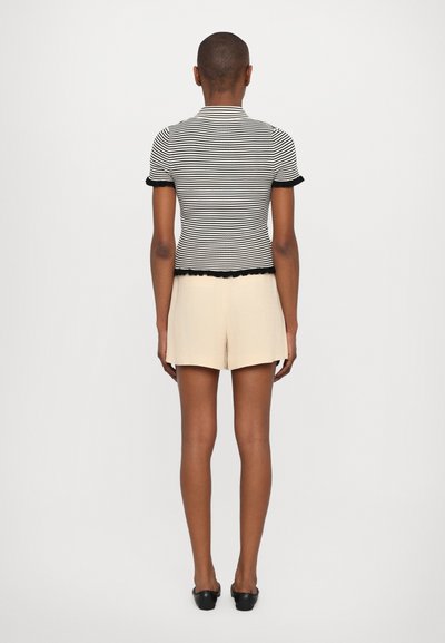 Top ajustado de rayas blancas y negras con mangas cortas y bordes en forma de ondas, combinado con pantalones cortos beis claros, visto desde la espalda.