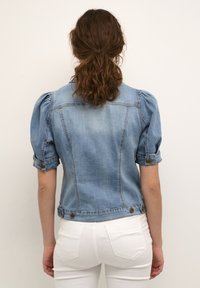 Giacca di jeans azzurro chiaro con maniche a sbuffo, polsini con bottoni e un design cropped. Presenta tasche e una texture leggermente consumata.