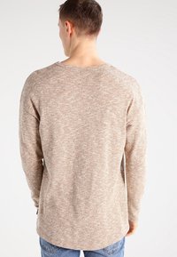 Svetr s dlouhým rukávem v světle hnědé a krémové skvrnité vzoru. Má zaoblený výstřih a uvolněný střih. Hladká textura.