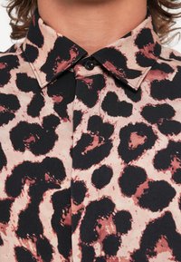 Leopard-print shirt featuring a black and pink color scheme, button-down collar, and textured fabric with a prominent pattern.