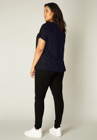Zwarte, loszittende top met korte mouwen en een ronde halslijn, gecombineerd met strak zittende zwarte leggings en witte sneakers.