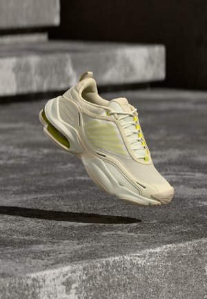 Baskets de sport beiges et jaunes à semelle rembourrée suspendues au-dessus de marches en béton texturé en plein air.