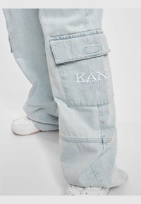 Pantalones cargo de mezclilla azul claro con un corte holgado, que cuentan con bolsillos laterales, un logo bordado en la pierna y dobladillos ajustados.