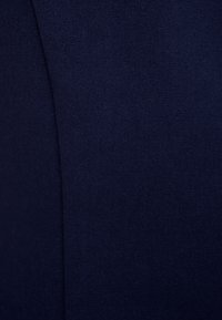 Granatowy materiał o gładkiej fakturze i subtelnym połysku. Posiada dopasowany szew biegnący pionowo, co nadaje mu zorganizowany wygląd.