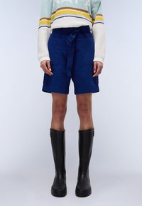 Bermuda in lino blu navy con vita regolabile, dotati di una vestibilità rilassata e orli risvoltati, abbinati a stivali di gomma neri al ginocchio.