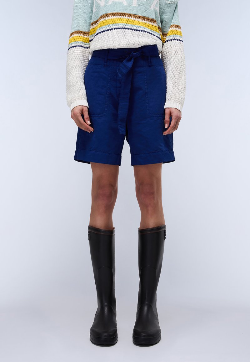 Bermuda in lino blu navy con vita regolabile, dotati di una vestibilità rilassata e orli risvoltati, abbinati a stivali di gomma neri al ginocchio.