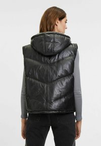 Schwarze gepolsterte Weste mit Kapuze, die ein gestepptes Design, eine glänzende lederähnliche Textur und Zickzack-Nähte aufweist. Rückansicht abgebildet.