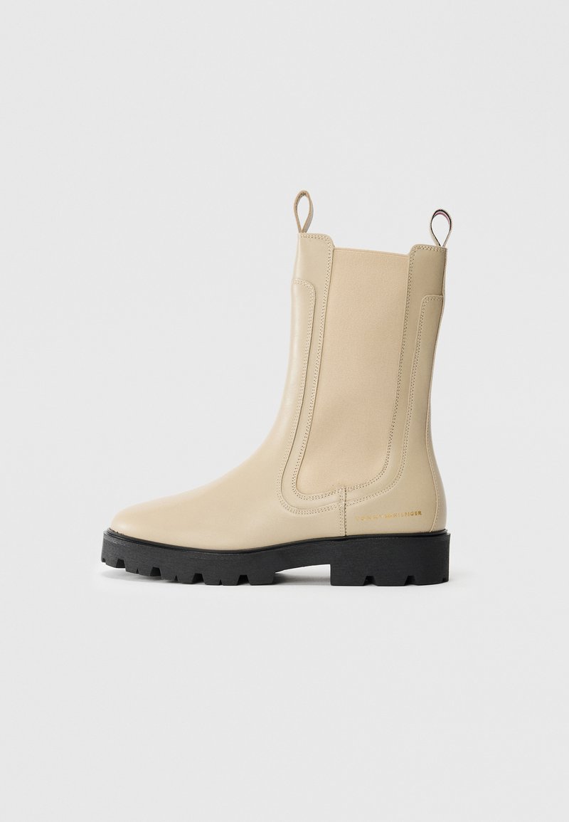 Bota Chelsea de cuero beige con suela de granulado negra, paneles laterales elásticos, lengüetas y un discreto logotipo dorado en el talón.