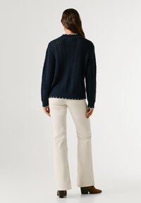 Tumesinine kootud sviiter tekstureeritud nööride mustriga, ribiklappidega ja laineline äär, sobitatud koorevärvi laienevate püksidega.