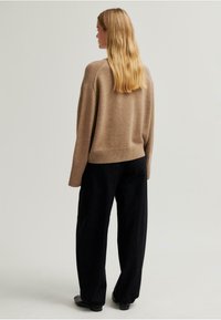 Világosbarna gyapjú pulóver bordázott részletekkel, fekete, bőszárú nadrággal párosítva. Simább textúra, laza fazon és minimalista dizájn.