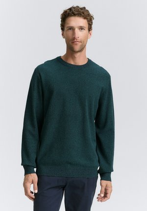 Suéter de punto texturizado en verde con mangas largas, escote redondo y puños y dobladillo acanalados. Se lleva con pantalones oscuros sobre un fondo claro.