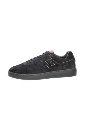 Zwarte suède lage sneaker met zwarte veters, een dikke zwarte zool en een gestikt geometrisch logo aan de zijkant.
