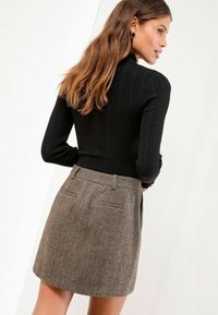 Sort ribbet turtleneck sweater parret med en brun herringbone nederdel. Nederdelen har lommer og et tætsiddende taljebånd.