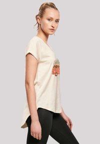 Lichtbeige T-shirt met korte mouwen featuring een kleurrijke vintage bus graphic met bloemetjesaccenten. Boogvormige zoom. Draag het met zwarte leggings.