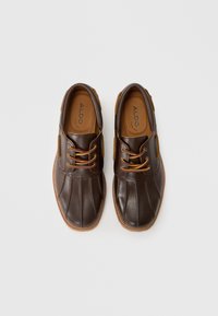 Brown leather shoes with a rounded toe, contrasting tan laces, side panels, and a decorative stitched sole. "ALDO" branding on the insole.