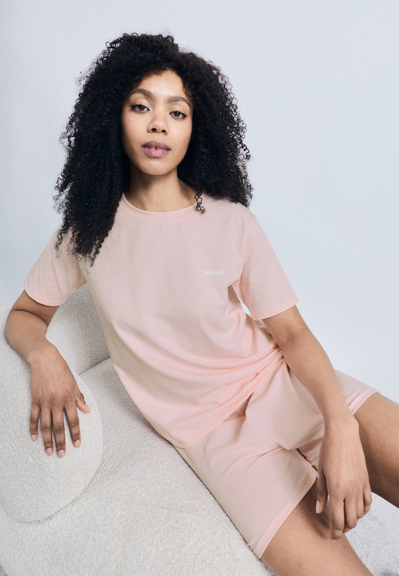 Απαλό ροζ κοντομάνικο μπλουζάκι με διακριτικό λογότυπο "HUGO", συνοδευόμενο από ταιριαστό σορτς. Μαλακή, λεία υφή υφάσματος.