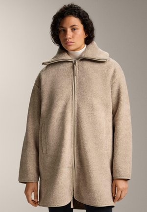 Beige oversized fleece coat with a high collar, front zipper, and side pockets; soft texture and relaxed fit.