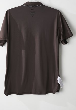 T-shirt de sport Nike manches courtes marron foncé suspendu, montrant le dos, avec le texte "NIKECOURT" à l'intérieur du col et une étiquette d'entretien visible sur le côté droit.