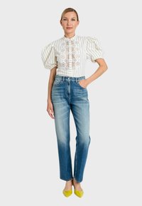 Blusa bianca a righe con maniche a sbuffo e ritagli floreali, abbinata a jeans in denim azzurro a vita alta e ballerine gialle a punta.