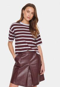 Top de punto a rayas burdeos y gris con mangas cortas, combinado con una falda de cuero granate con diseño plisado y bolsillos frontales.