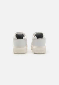 White and black leather sneakers with a textured sole, rounded toe, and visible brand logo embossed on the heel.