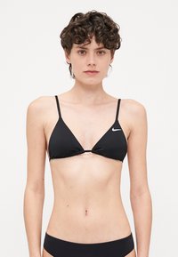 Svart triangulär bikiniöverdel med tunna spaghettiband, med en liten vit Nike-logga i mitten. Slät tyg, minimalistisk design.