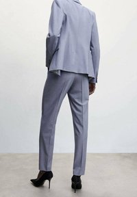 Light gray tailored suit consisting of a fitted blazer and slim trousers, paired with black high-heeled shoes. Smooth fabric texture.