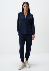 Felpa blu navy con scollo a V e maniche lunghe, abbinata a pantaloni jogger a gamba stretta. Presenta un tessuto morbido e polsini a costine.
