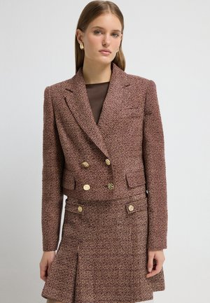 Blazer cropped à double boutonnage en tissu texturé bordeaux avec des boutons dorés et deux poches avant, associé à une jupe assortie.