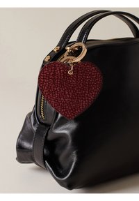 Sac en cuir noir avec une fermeture éclair et des accessoires en or, doté d'un porte-clés en cuir en forme de cœur rouge foncé texturé attaché à la poignée.