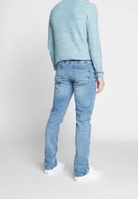 Jeans de mezclilla azul claro, ajustados, con un acabado desgastado, cinco bolsillos y detalles de costura sutiles. La vista trasera muestra un suéter a juego.