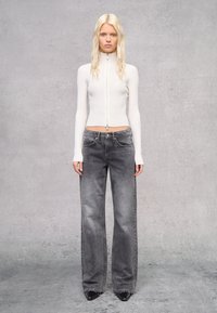 Top zip-up bianco a coste abbinato a jeans grigi a gamba larga. Tessuto testurizzato con una silhouette aderente e tasche frontali piatte. Scarpe nere a punta.