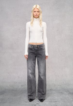 Witte geribbelde zip-up top gecombineerd met grijze wijde jeans. Gestructureerde stof met een aansluitende pasvorm en vlakke voorzakken. Zwarte puntige schoenen.