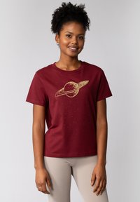 Bordeaux katoenen T-shirt met een gouden afbeelding van Saturnus met ringen en kleine steraccenten; ronde hals en korte mouwen.