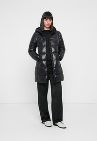 Zwarte pufferjack met een capuchon, met een glanzende afwerking, ritssluiting en stikseldetails. Gestyled over een zwarte top en broek.