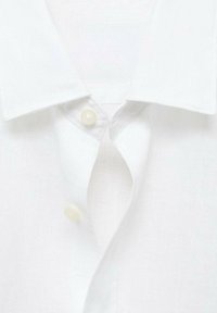 Camisa de lino blanca con un cuello clásico, que cuenta con un tapeta con dos botones. La textura es ligeramente arrugada, lo que resalta su estilo casual.
