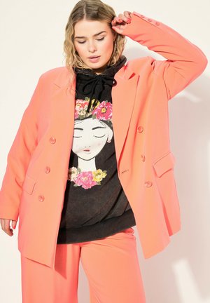 Coral oversized blazer with double buttons, worn over a black hoodie featuring floral graphic. Smooth texture with relaxed fit.