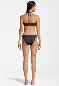 Conjunto de bikini negro que presenta un top con lazo al cuello y una parte inferior de cintura baja. La tela tiene un patrón de logo en relieve. Textura suave, diseño minimalista.