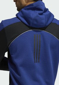 Hoodie de sport bleu avec une finition texturée, des accents noirs sur les épaules et trois rayures verticales noires au dos pour le branding.