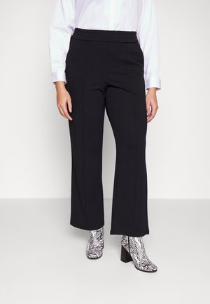 Person trägt schwarze, gerade geschnittene Hose und weißes, langärmliges Hemd, kombiniert mit schwarz-weißen, zebra gemusterten, hochhackigen Stiefeletten.