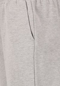 Helle graue Jogginghose mit elastischem Bund, Seitentasche und strukturiertem Stoff. Mit geprägt auf der Seite versehenem Branding.