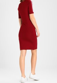 Czerwona dzianinowa sukienka z krótkimi rękawami, z białymi paskami po bokach. Dopasowany krój, sięgający do połowy uda, w zestawieniu z białymi sneakersami.