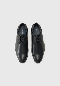 Zapatos de cuero negro con un acabado suave, punta redondeada y diseño de cordones que cuentan con paneles laterales texturizados. Nombre de la marca visible en el interior.