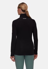 Maglia in fleece nera a maniche lunghe con colletto alto, caratterizzata da cuciture piatte e logo riflettente. Texture liscia con un design aderente.