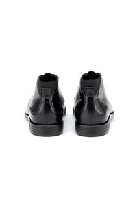 Schwarze Lederstiefeletten mit elastischen Seiteneinsätzen und einer strukturierten Sohle, mit glatter Oberfläche und dezentem Branding auf der Rückseite.